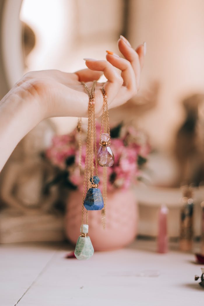 Aesthetic close-up of a woman's hand holding crystal jewelry against a floral background.