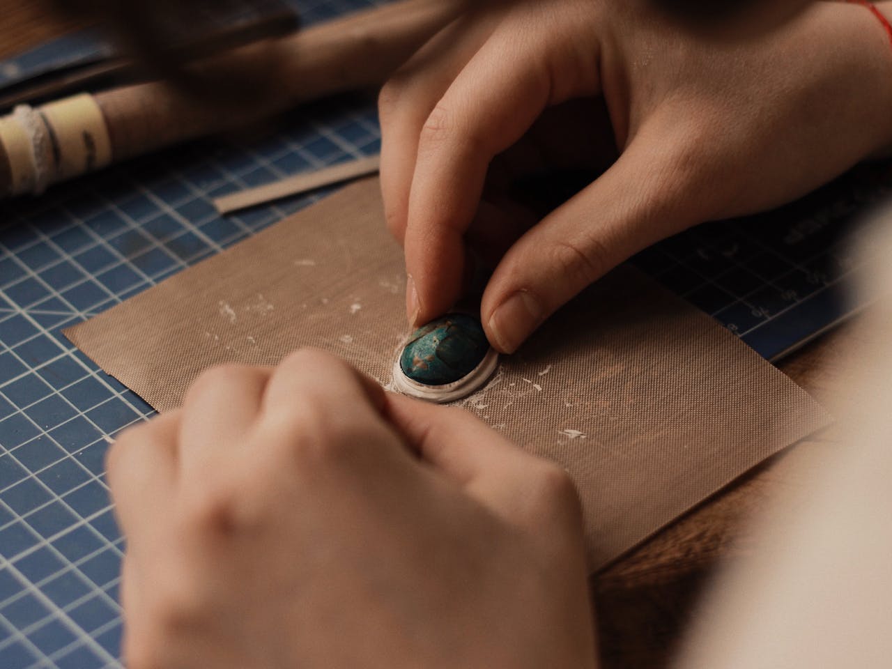 Detailed view of hands crafting jewelry with turquoise gemstone, emphasizing precision and artistry.