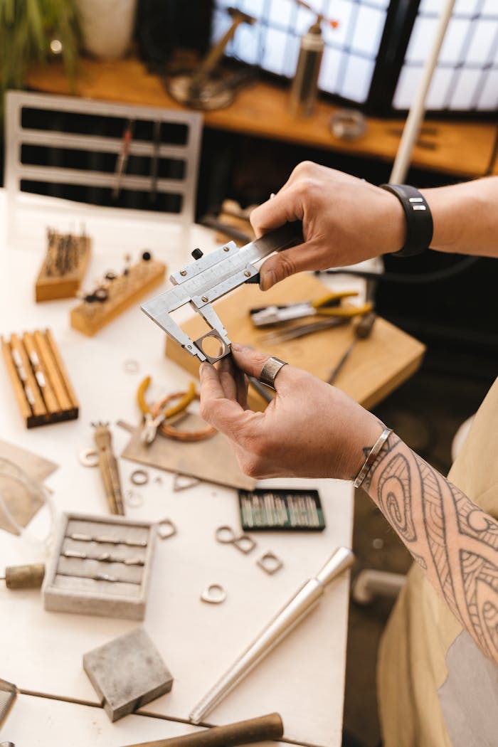 Close-up of hands crafting jewelry with tools on a workshop table, showcasing intricate craftsmanship.