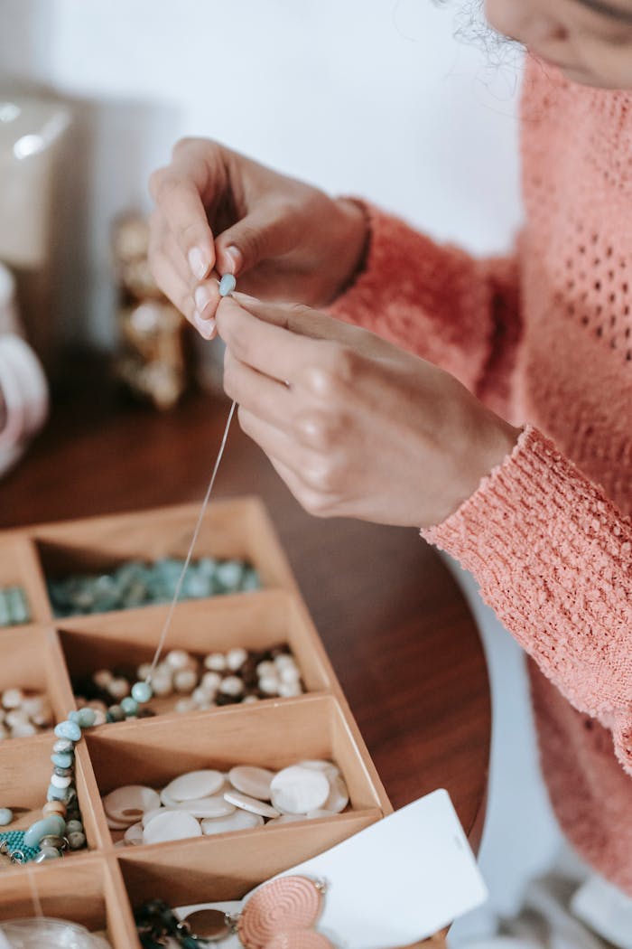 Anonymous female arranging beads and blue natural stones on fishing line while doing handmade bijouterie